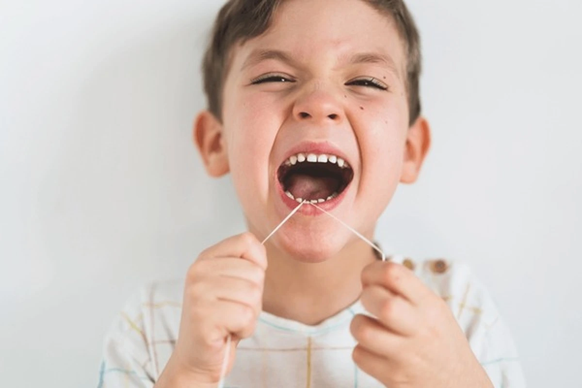 Baby root canal Frisco TX: joyful boy grinning wide while flossing teeth for healthy gums at Dental Smart Kids