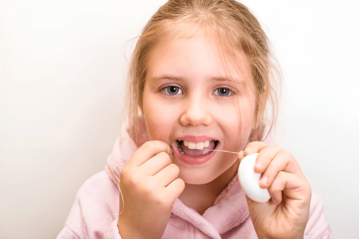 Kid-friendly oral hygiene demo: Young girl flossing during a routine checkup to support early oral cancer screening and prevention at Dental Smart Kids in Frisco, TX