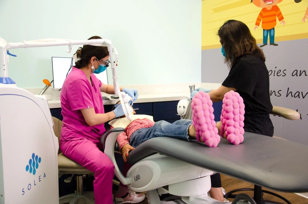 "Fun, safe teeth whitening for kids at Dental Smart Kids in Frisco, TX: Little girl in cozy pink slippers gets a bright smile treatment in a playful pediatric office