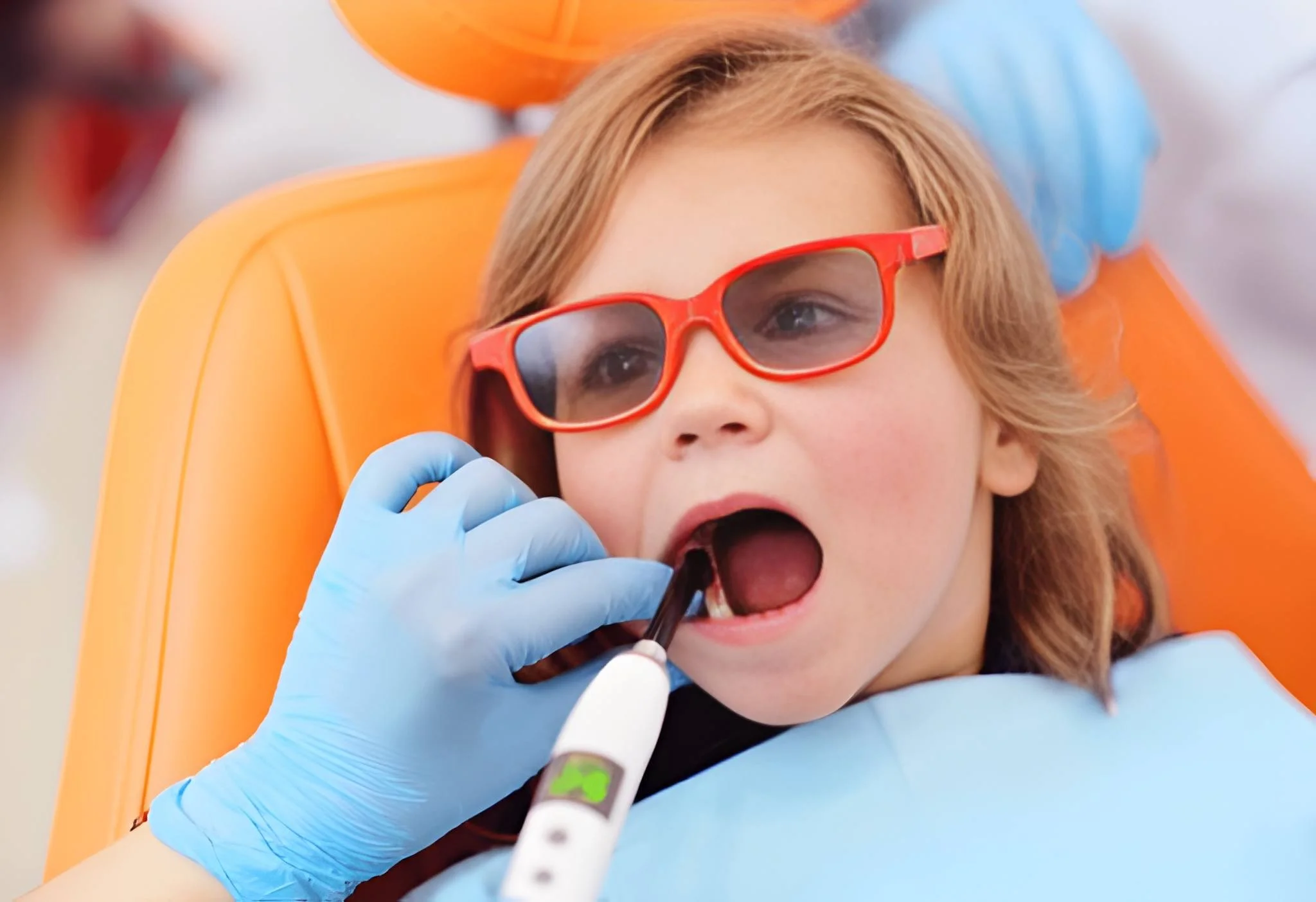 Pediatric oral surgery Frisco TX: girl with red glasses in gentle procedure with electric handpiece at Dental Smart Kids
