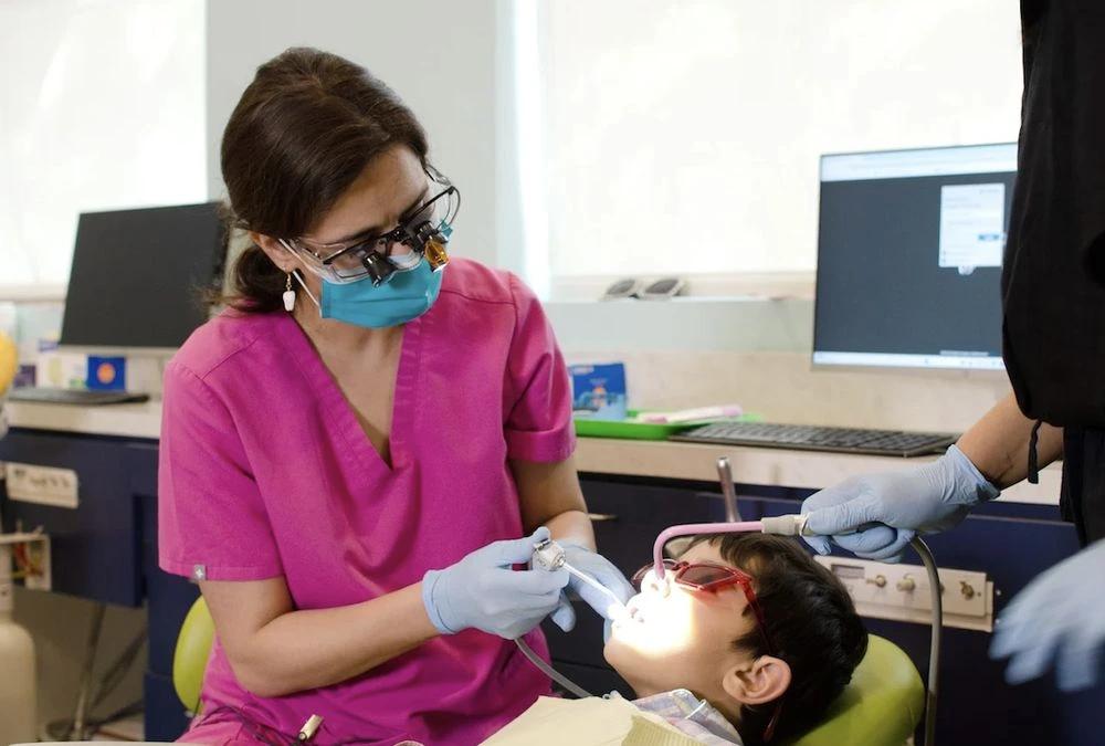 Pediatric pulpotomies Frisco TX: assistant using handpiece on boy with sunglasses in gentle pulp care at Dental Smart Kids