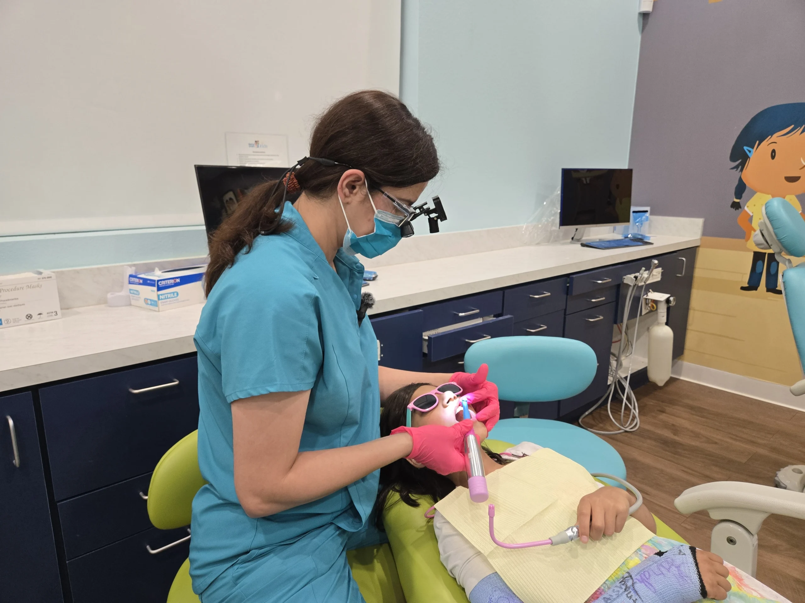 Oral cancer screening in action at Dental Smart Kids in Frisco, TX: Female dentist using magnification glasses and tool to check a smiling young patient's teeth for early detection